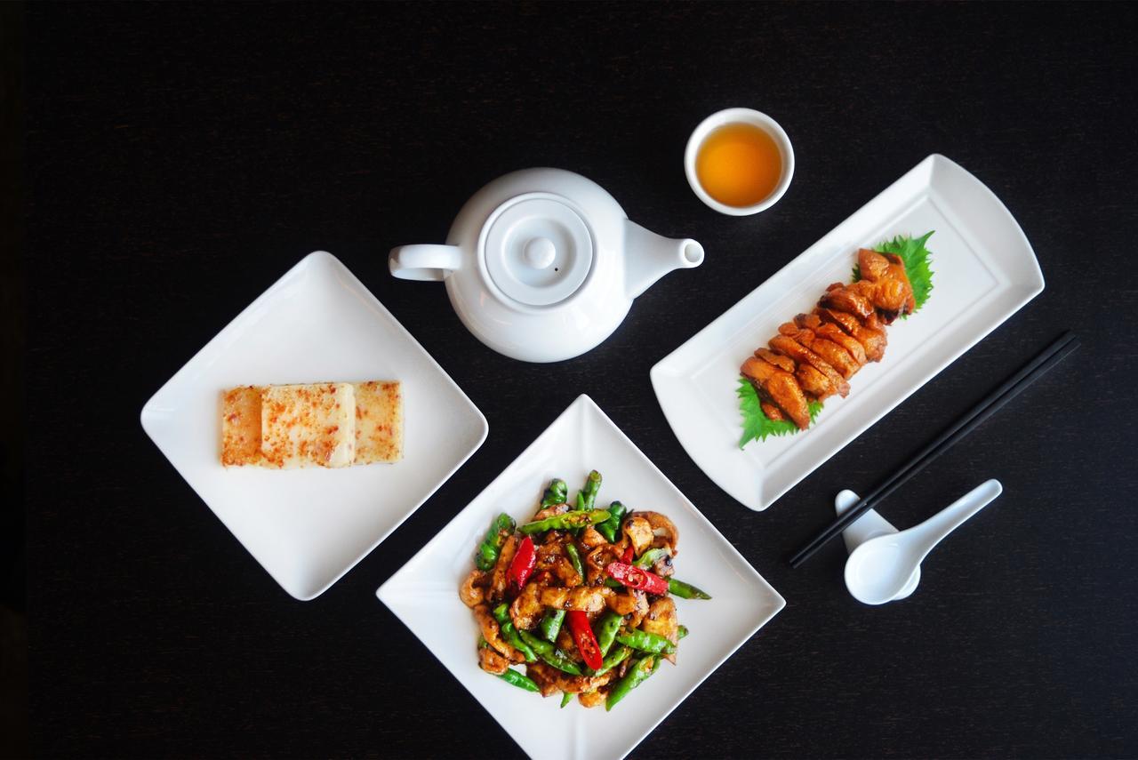 Caesar Metro Taipei Ξενοδοχείο Εξωτερικό φωτογραφία The photo features a stylish arrangement of Asian cuisine on a black surface. It includes:

1. **Teapot**: A white teapot positioned with a small cup of tea next to it.
2. **Main Dishes**:
   - A rectangular plate with slices of chicken, likely marin