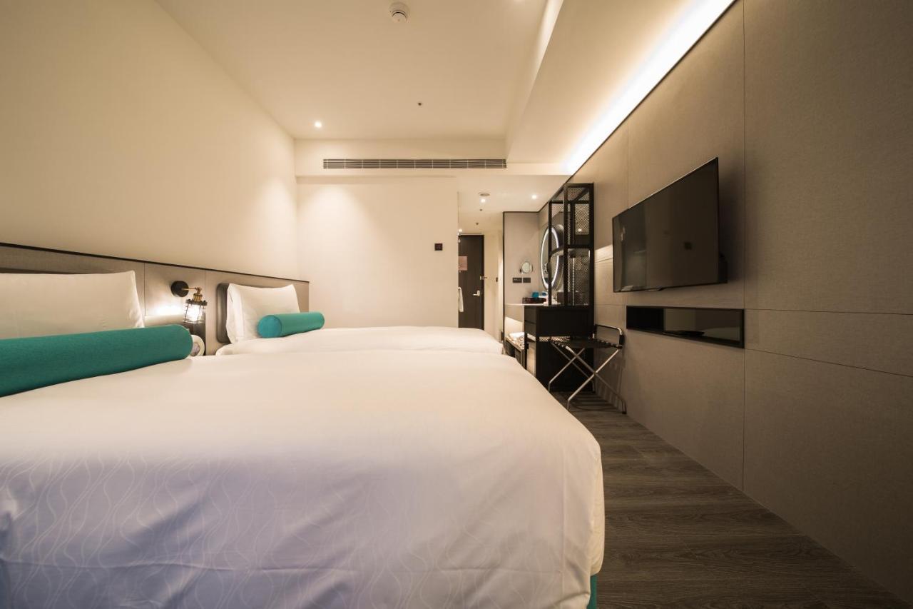 Caesar Metro Taipei Ξενοδοχείο Εξωτερικό φωτογραφία The photo shows a modern hotel room featuring two beds with white linens and teal accents. The walls are a light, neutral color, contributing to a clean and contemporary aesthetic. There is a minimalist design, with a mounted flat-screen TV on one wa
